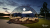 12m Outdoor Perspex dome at dusk with large glass light in the ceiling, dining tables around the edge and a piano on a large stage
